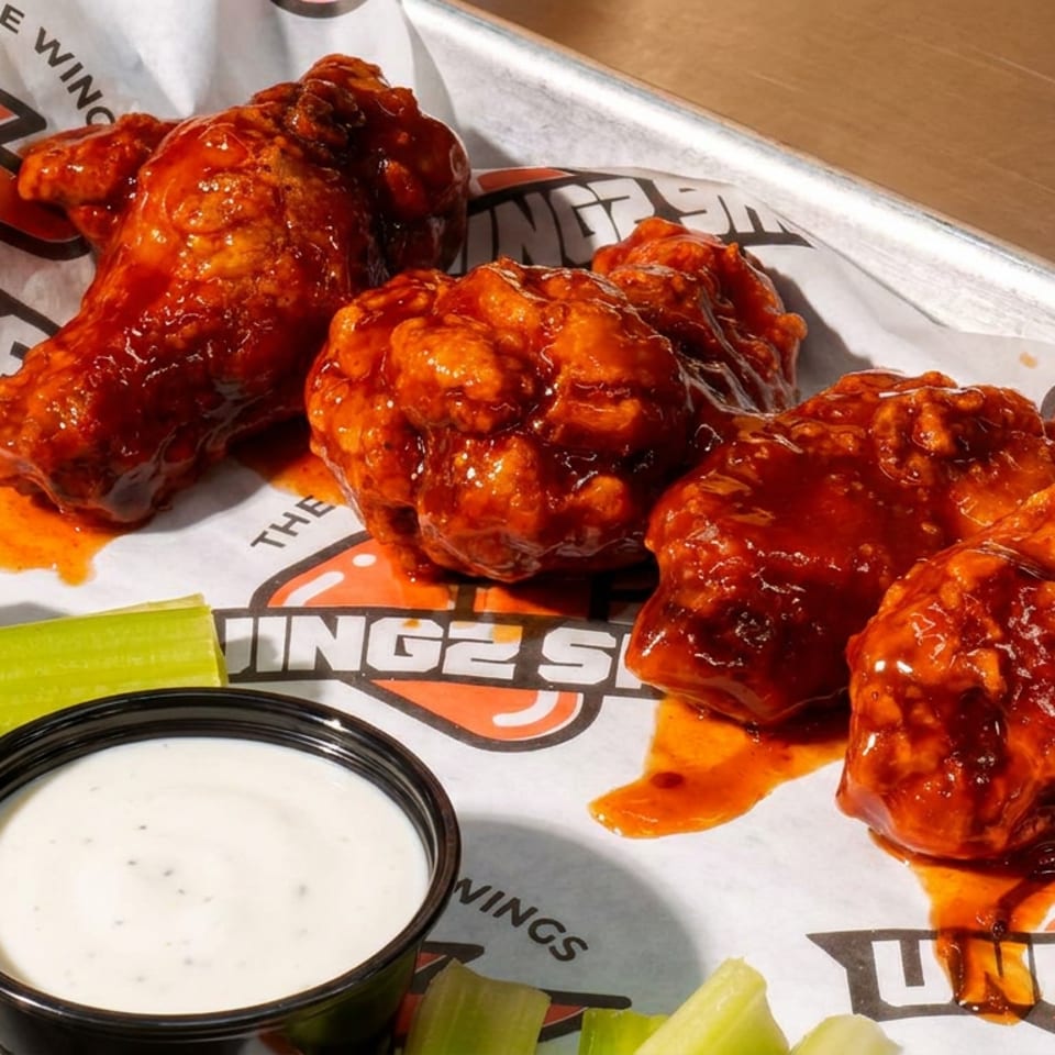 Spicy chicken wings with celery and ranch dip on Wingz Shack branded paper.